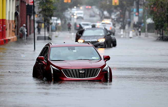 A car driving through a flooded street in New York City after a large storm.