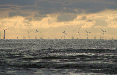 Ocean landscape with many wind turbines running along the horizon.