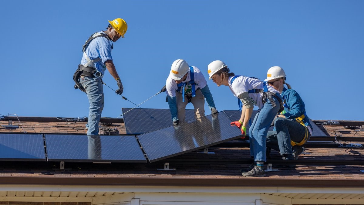 Clean Energy in Action: A team of four men and women install solar panels on the roof of a house.