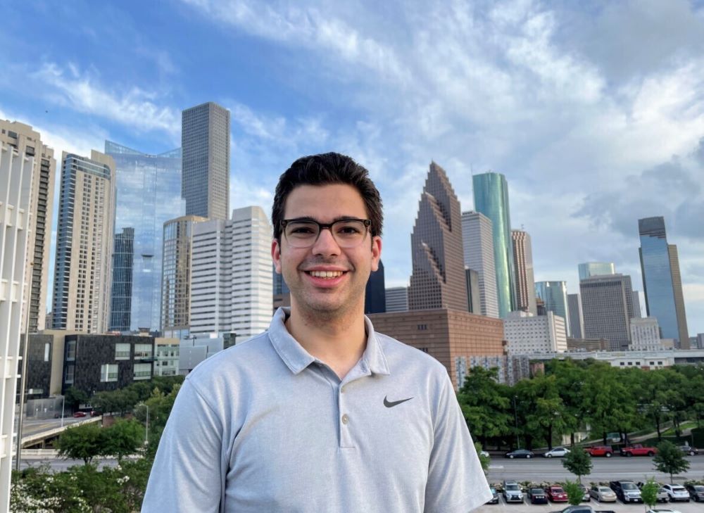 A young man smiles with a view of the Houston skyline in the background.