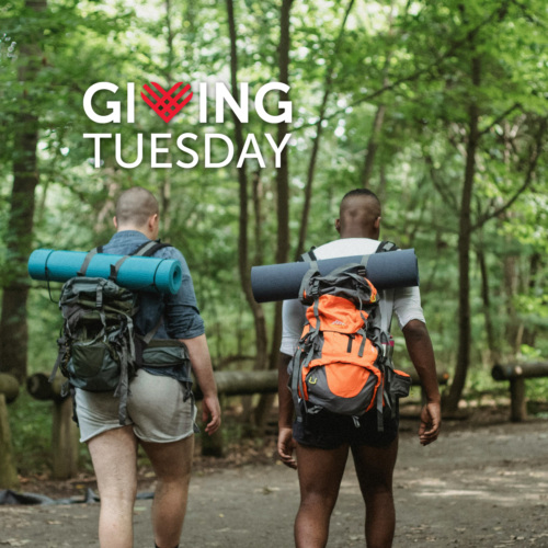 Two backpackers hiking in the woods with a "Giving Tuesday" logo in the upper left corner of the photo.