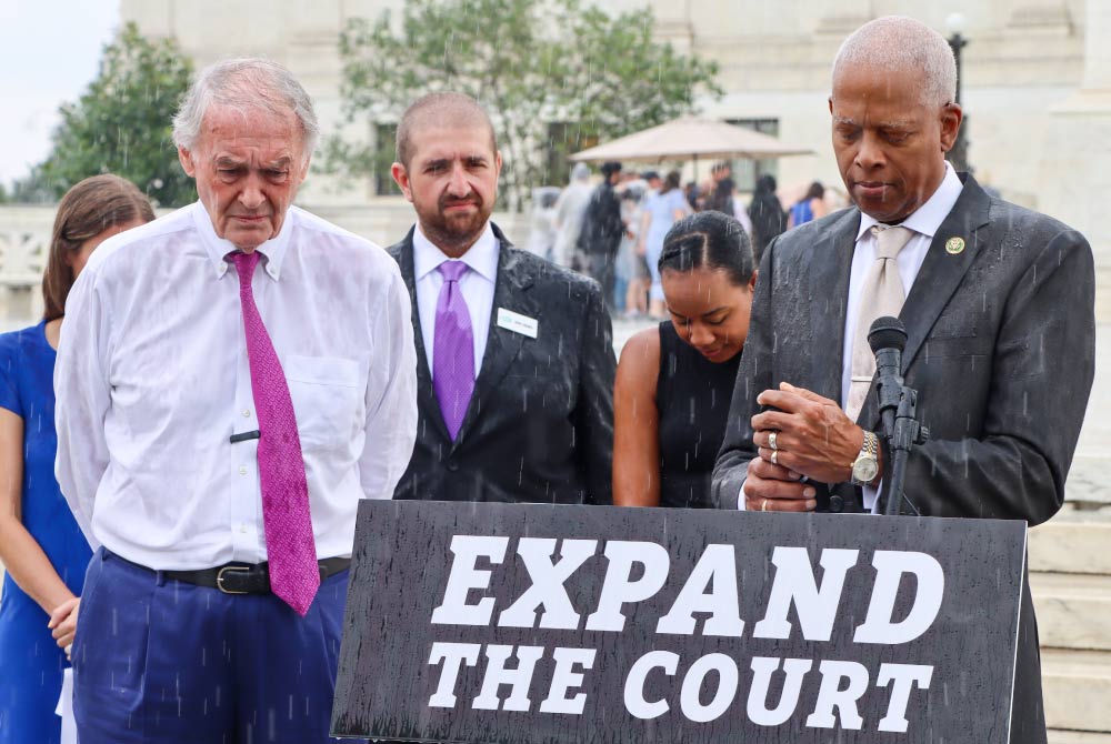 Representative Johnson speaks amid rain on the topic of Supreme Court expansion.